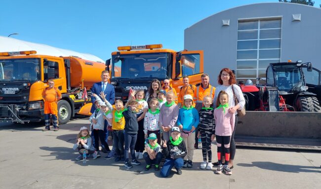 Grupa dzieci z nauczycielkami i pracownikami LIZUD na tle specjalistycznych pojazdów ZDiZ w Gdyni
