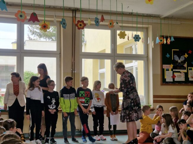 Na tle okien p. dyrektor wręcza grupie dzieci dyplomy.