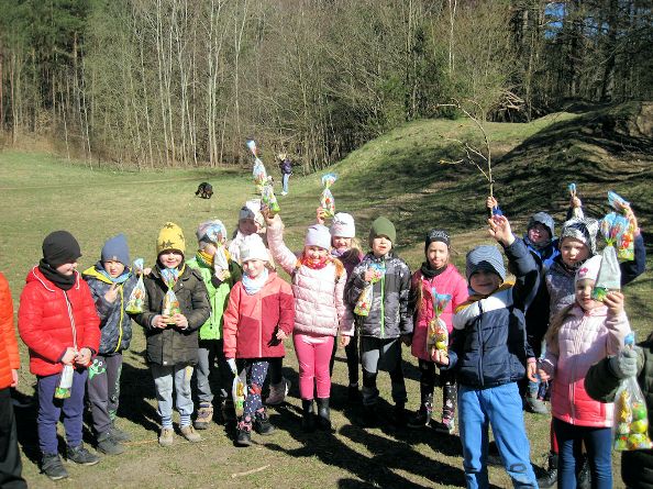 Dzieci z grupy 0 B pokazują na tle lasu znalezione prezenty