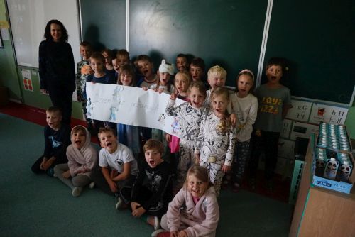 Dzieci z klasy 1c ubrane w piżamy z nauczycielką angielskiego na tle tablicy szkolnej