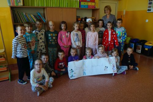 Dzieci z klasy 0a ubrane w piżamy z panią wychowawczynią na tle regałów szkolnych