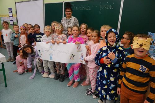 Dzieci z klasy 1a ubrane w piżamy z panią wychowawczynią na tle tablicy szkolnej