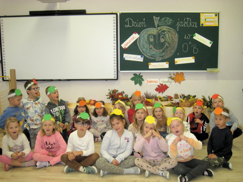 Zdjęcie grupowe 0 B pod tablicą z narysowanym uśmiechniętym jabłkiem i wypisanymi jego zaletami