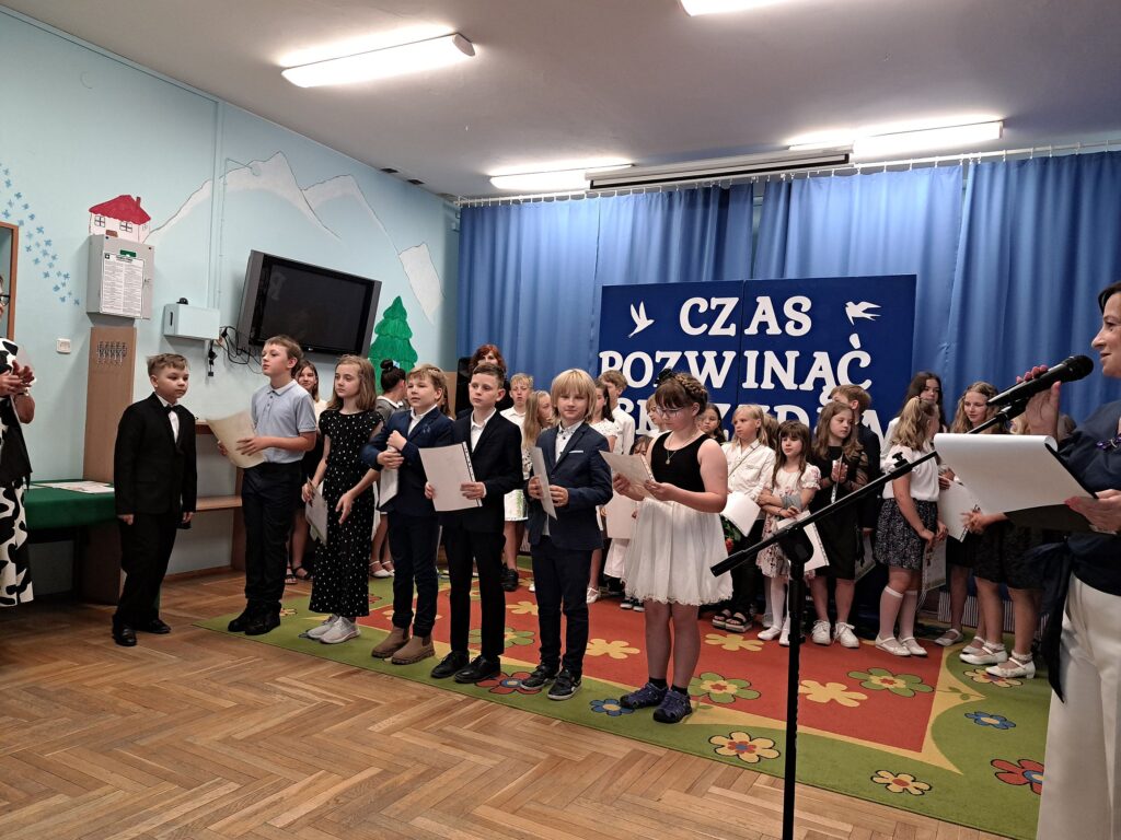 Uczniowie z klas trzecich pozują ze swoimi dyplomami na tle dekoracji z okazji zakończenia roku szkolnego