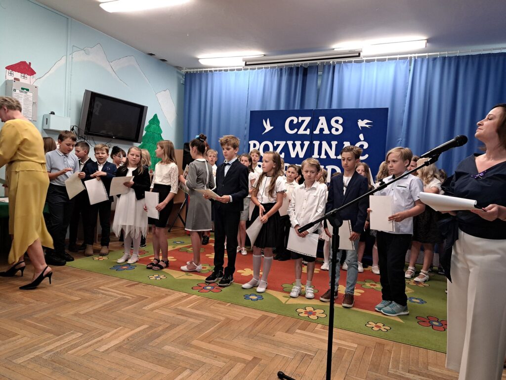 Uczniowie z klas trzecich pozują ze swoimi dyplomami na tle dekoracji z okazji zakończenia roku szkolnego